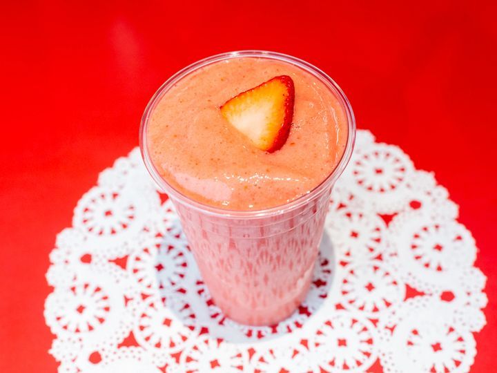 A strawberry smoothie in a plastic cup with a strawberry on top.