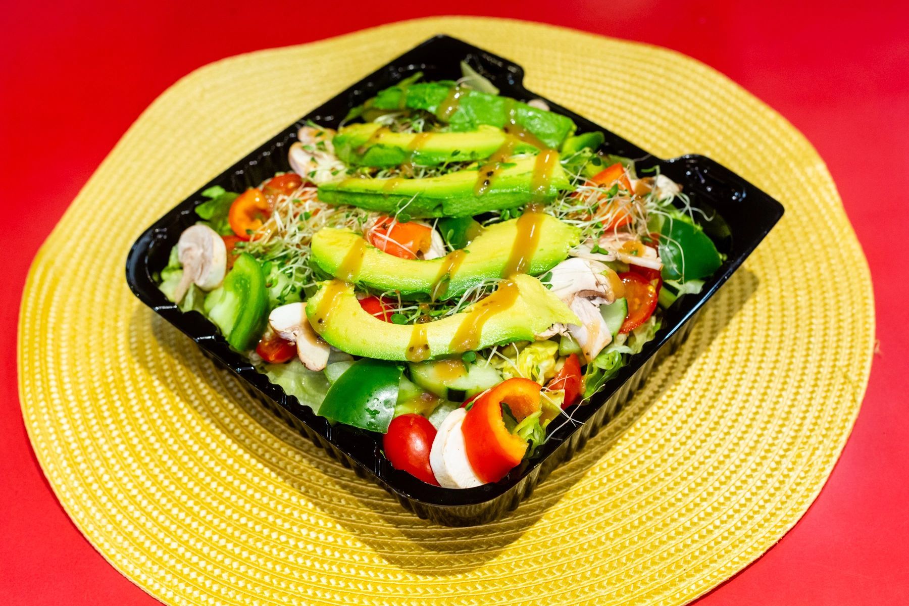 A salad in a plastic container is sitting on a yellow place mat on a table.