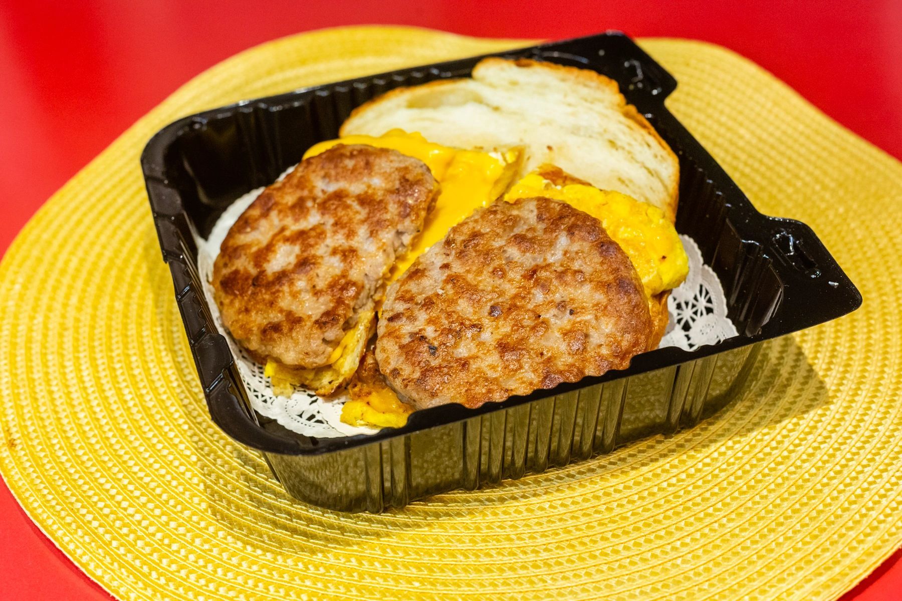 A plastic container filled with sausage and eggs on a yellow place mat.