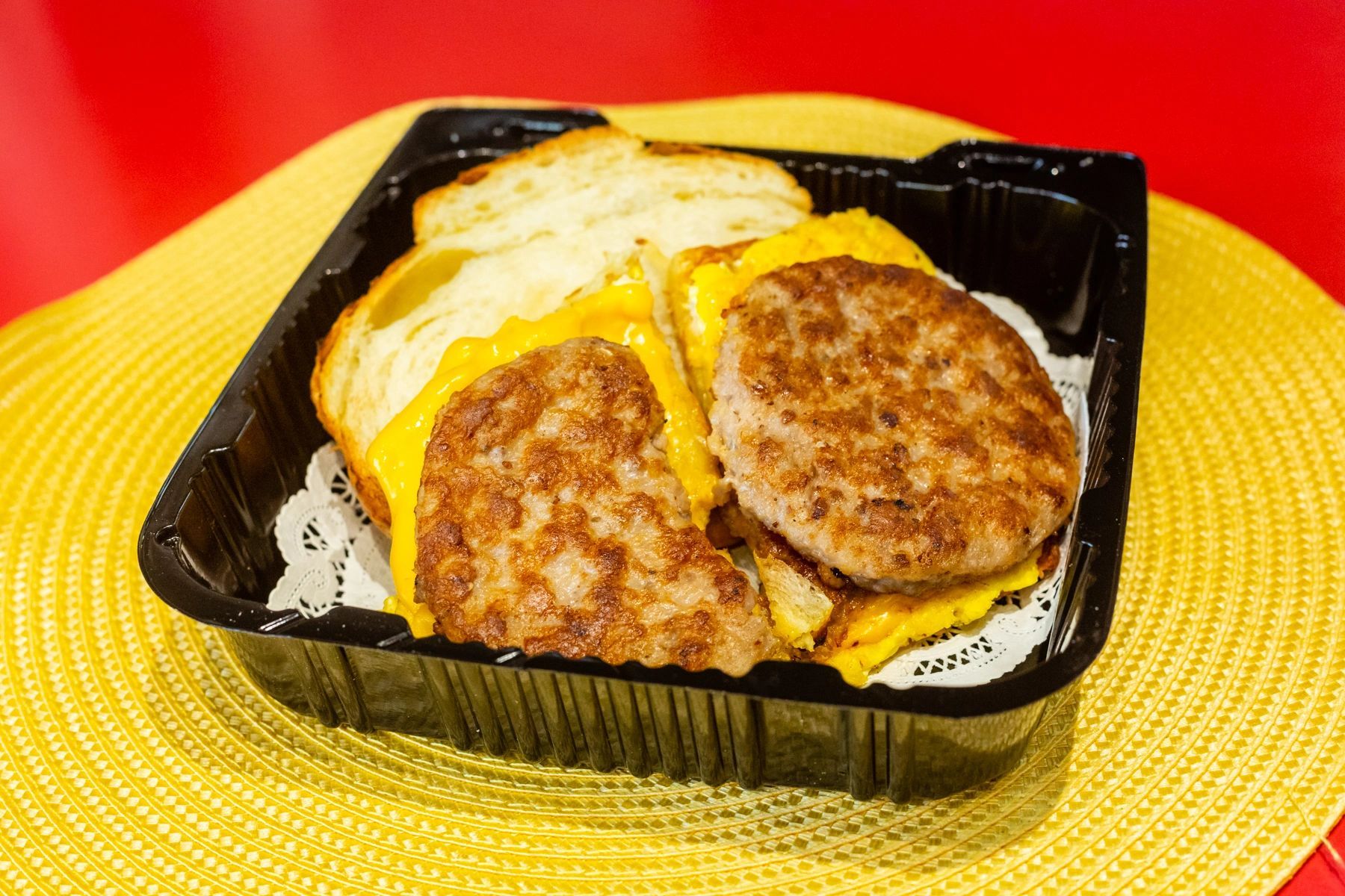 A sausage and egg sandwich in a plastic container on a yellow place mat.