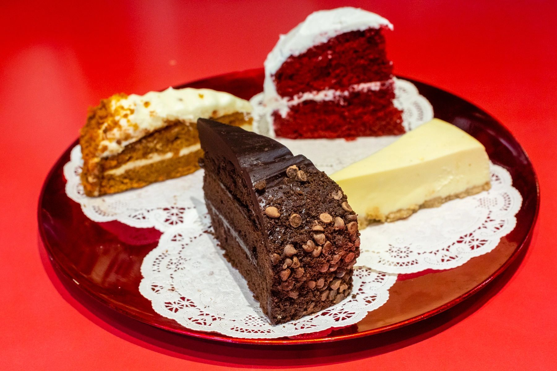Four different types of cakes are on a plate on a red table.