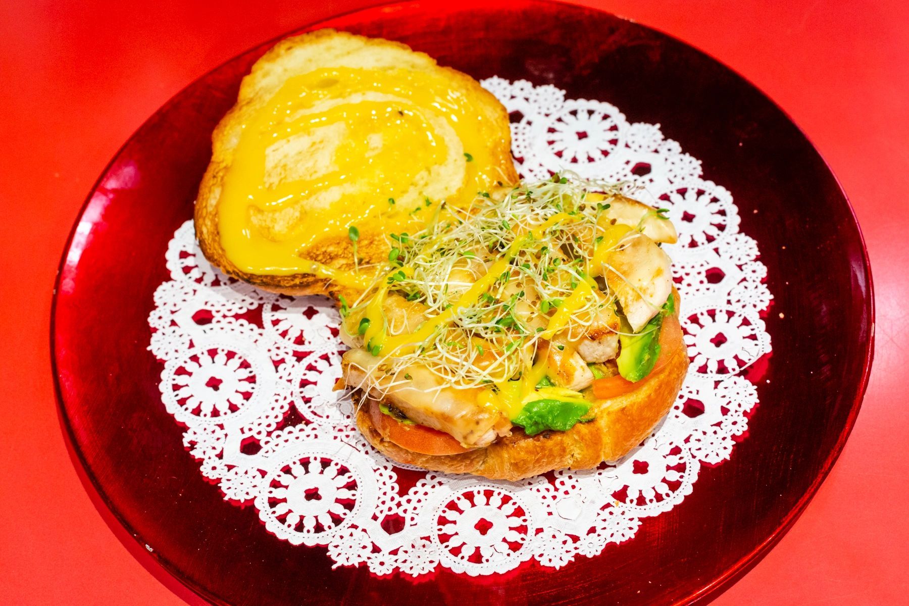 A sandwich on a red plate with a lace napkin