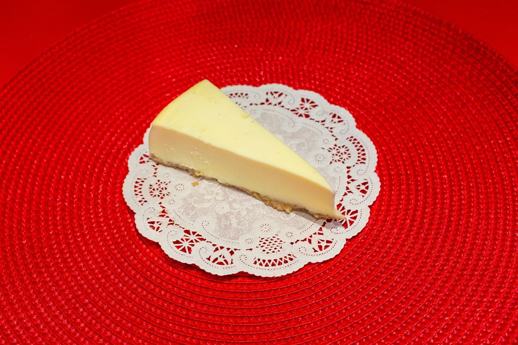 A slice of cheesecake is sitting on a red place mat.