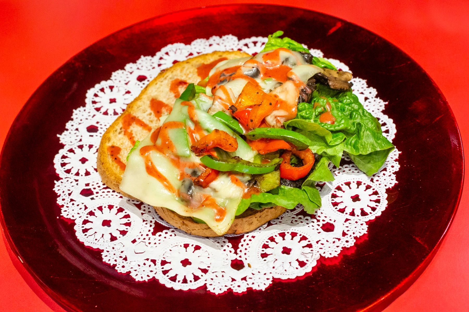 A red plate topped with a sandwich and vegetables on a lace napkin.