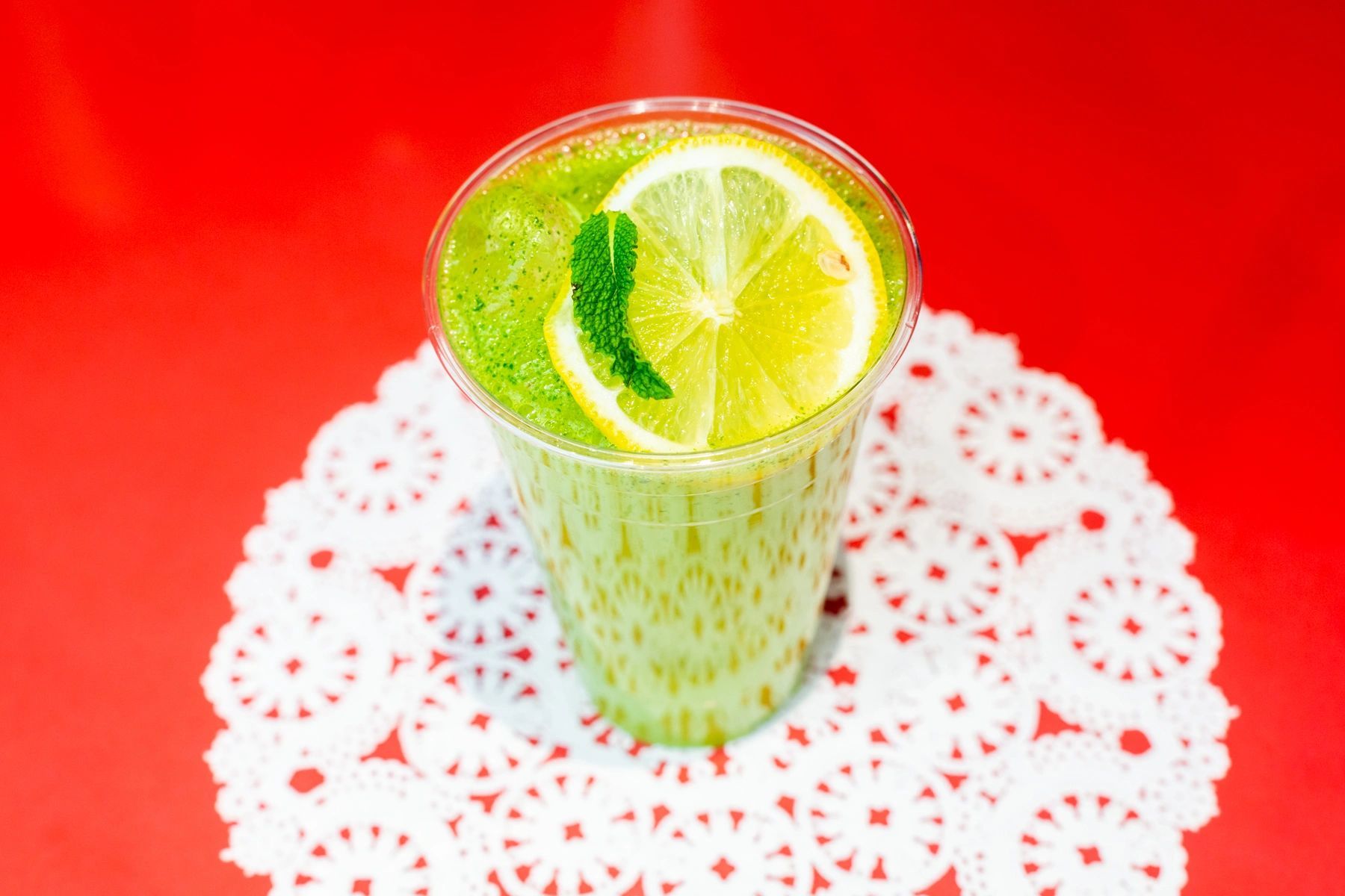 A green drink with a lemon slice and mint leaves in a plastic cup.