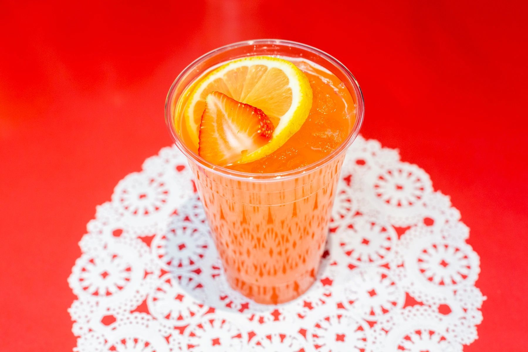 A cup of orange juice with a slice of lemon on a red table.