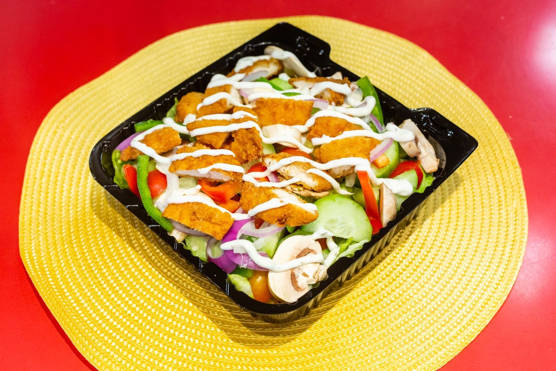 A salad with chicken and vegetables in a plastic container on a table.
