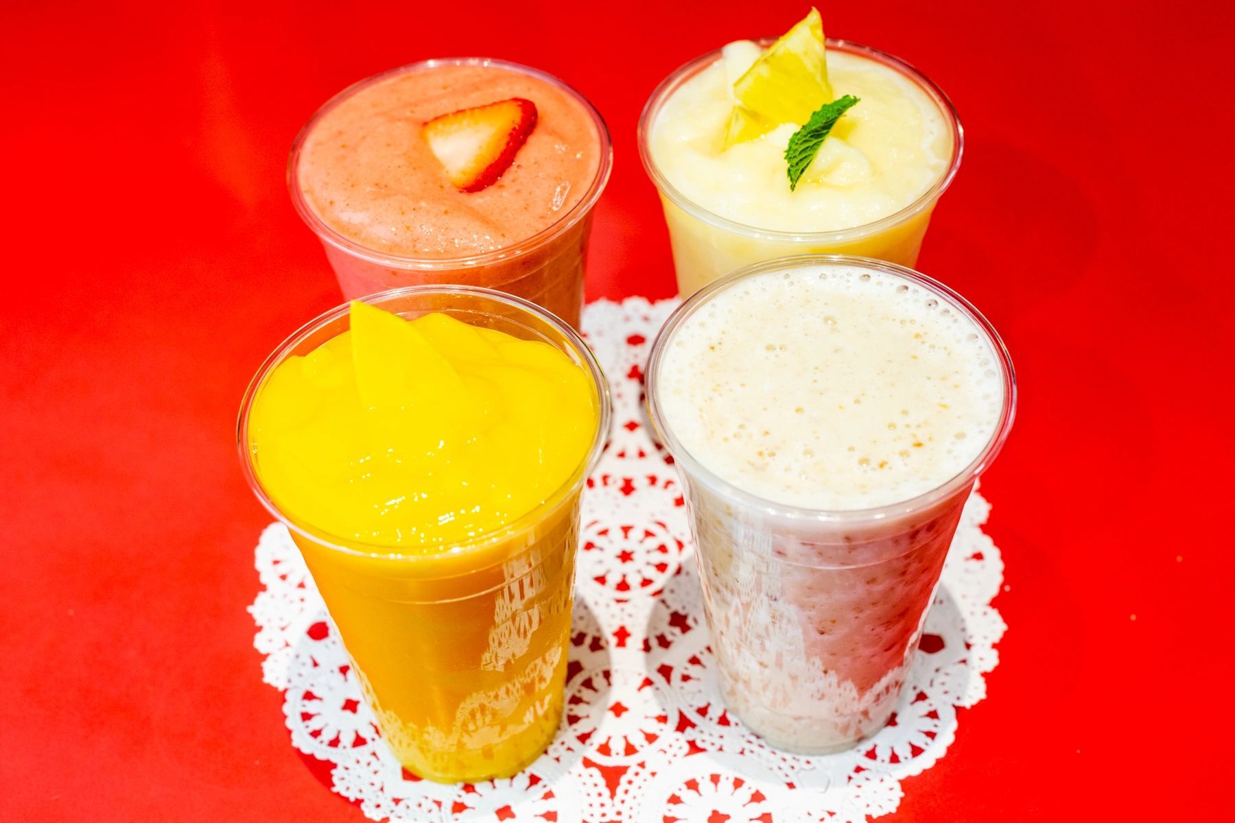 Four different smoothies are sitting on a red table.