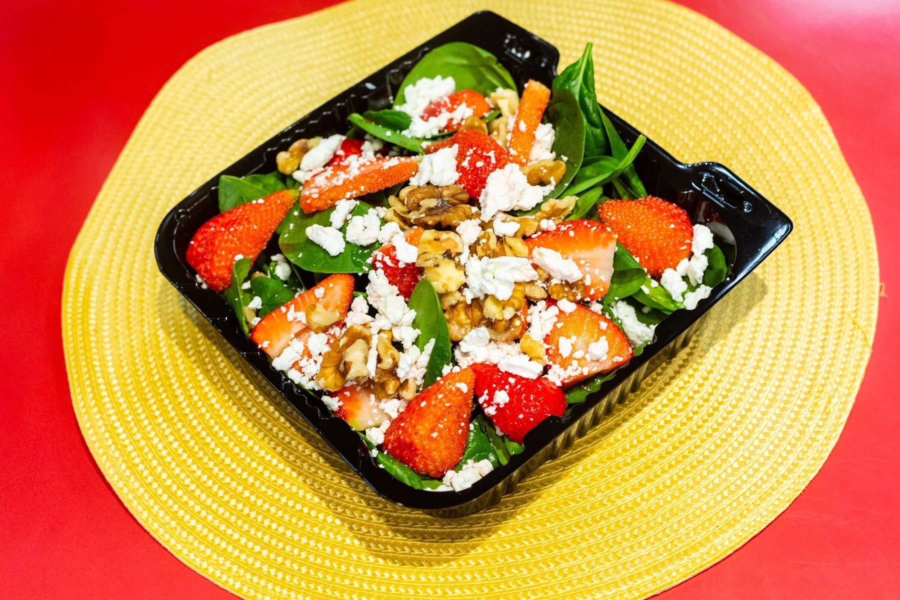 A salad with strawberries , spinach , feta cheese and walnuts is sitting on a yellow place mat on a table.