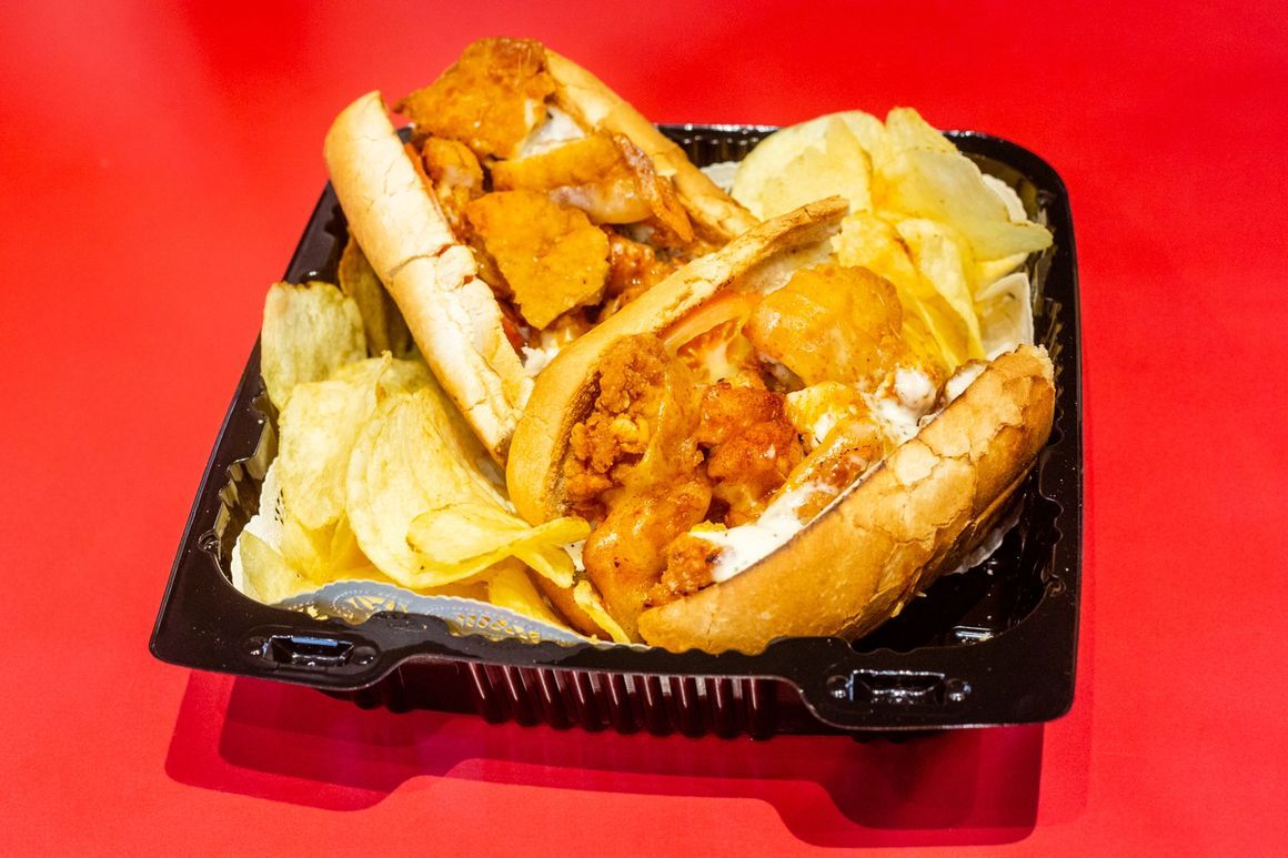 A sandwich and chips are in a plastic container on a red table.