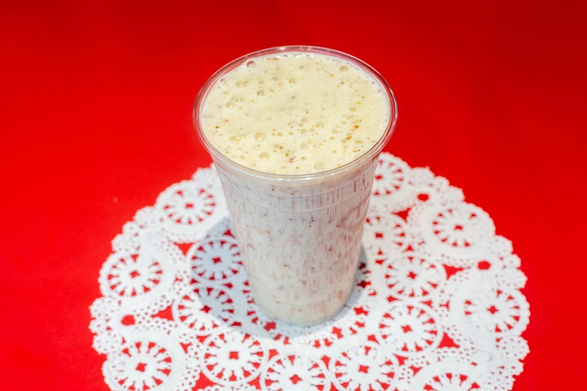 A smoothie in a plastic cup is sitting on a white doily on a red table.