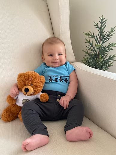 A baby is sitting on a couch holding a teddy bear