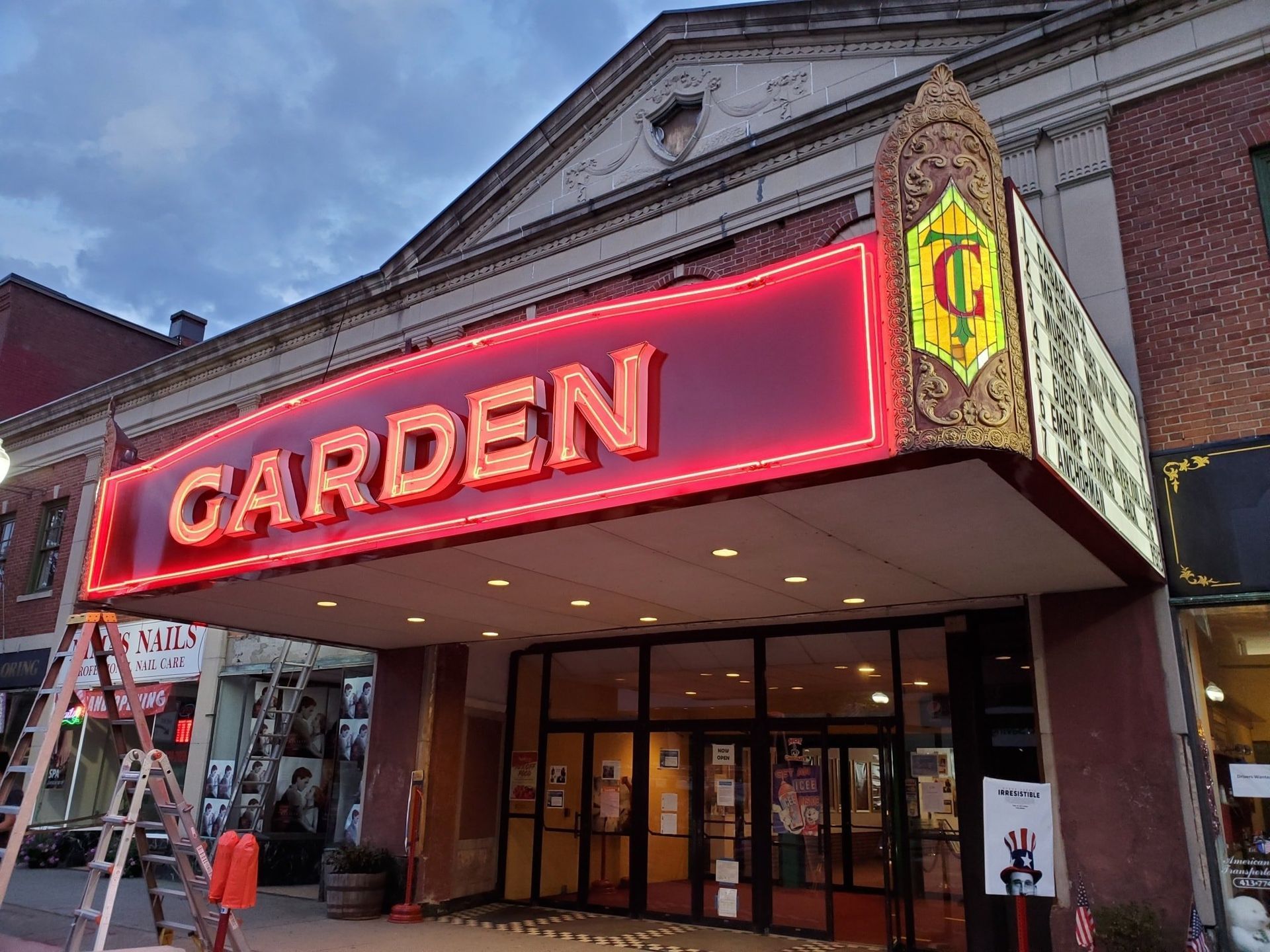 Garden Theater with red neon sign; brick building. Glass doors and small stage.