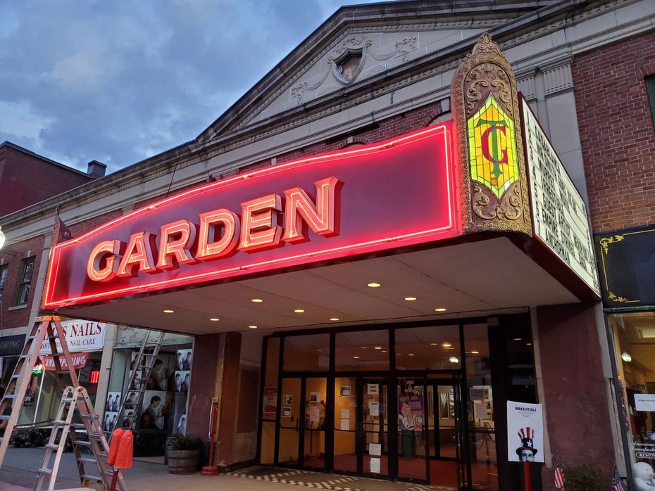 Garden Theater with red neon sign; brick building. Glass doors and small stage.