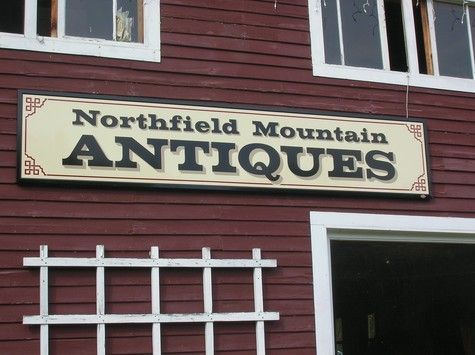 Sign for Northfield Mountain Antiques on a red building. Cream and black sign.
