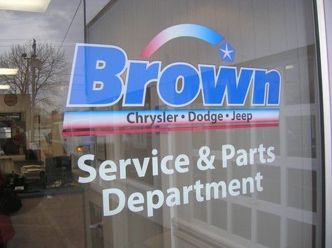 Sign on glass window: Brown Chrysler Dodge Jeep Service & Parts Department. Blue and white logo.