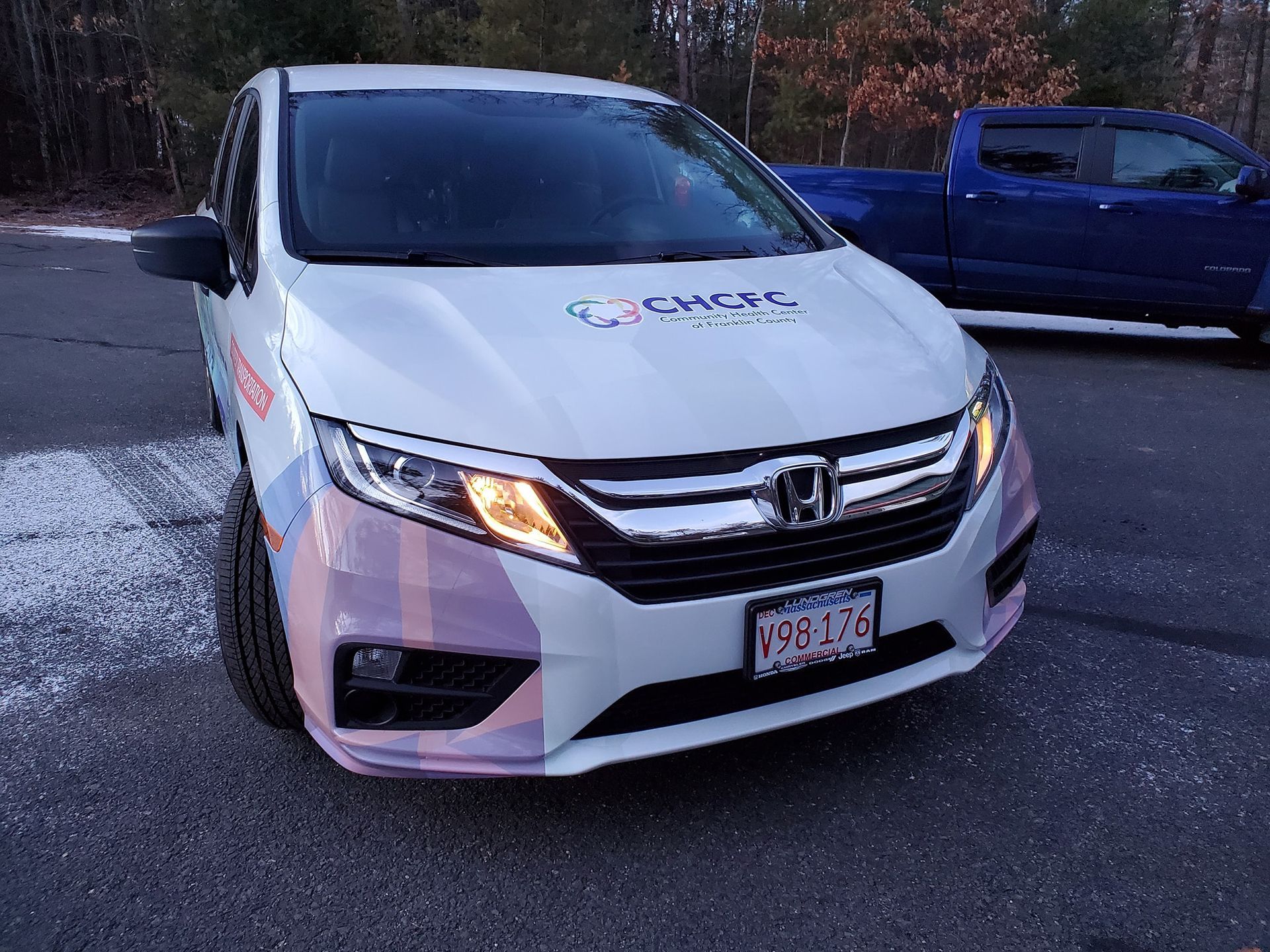 White minivan with logo, parked next to blue truck, license plate 