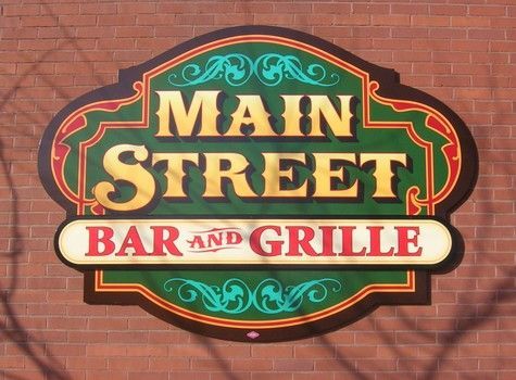 Sign for Main Street Bar and Grille, gold letters on green background, red border, brick wall.
