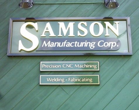 Sign for Samson Manufacturing Corp. in gold lettering on green background, with services