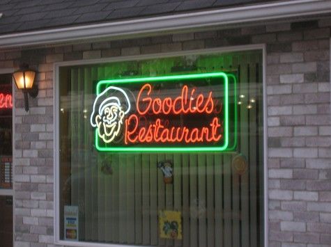 Neon sign for Goodies Restaurant; a smiling cartoon chef, red text, green outline, brick exterior.