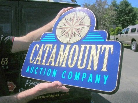 Person holding a blue CataMount Auction Company sign with a compass rose design; outdoors.