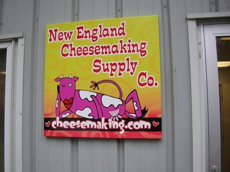 Sign for New England Cheesemaking Supply Co. features a pink cow reclining. Yellow background with red text and website.