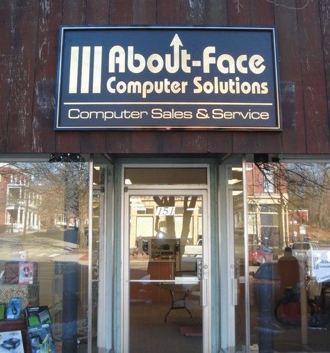Sign for About-Face Computer Solutions above a store entrance, with a storefront window reflecting the street.