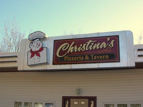Sign for Christina's Pizzeria & Tavern, featuring chef cartoon, red lettering, and white trim on a building.