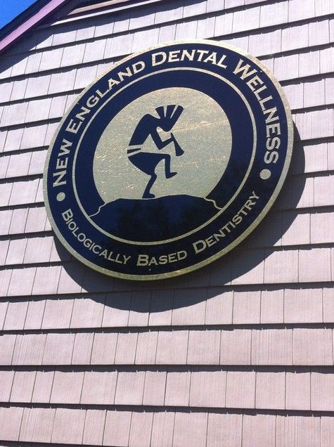 Round sign for New England Dental Wellness, featuring a dark-colored Kokopelli figure playing a flute. Gold and black colors.