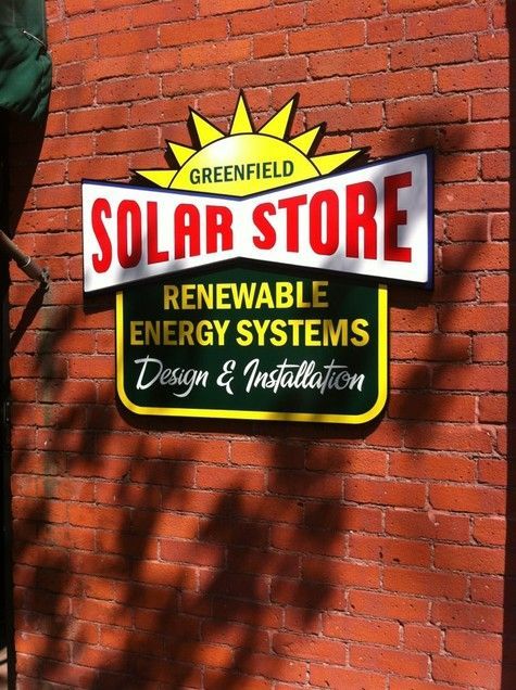 Sign for Greenfield Solar Store on a brick wall, with a sun logo and text.