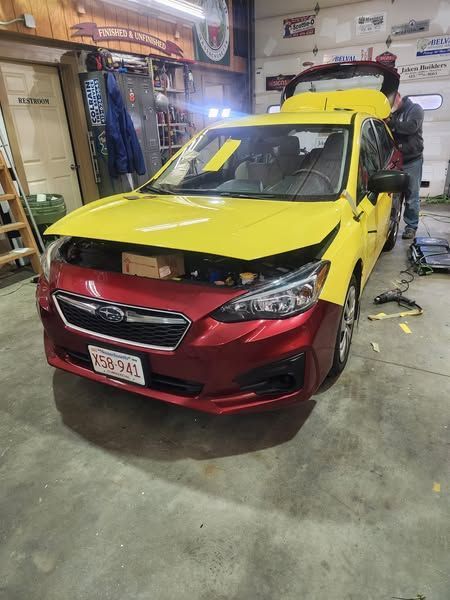 Yellow and red Subaru car being worked on in a garage, with a person in the background.
