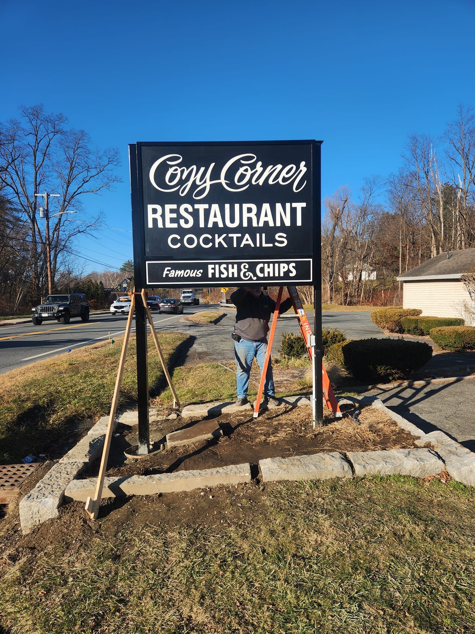 Sign for Cozy Corner Restaurant with a person working on it outside.