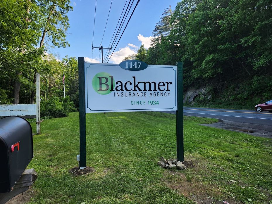 Blackmer Insurance Agency sign in front of a building, 1147. Green grass, dark green posts, and a road.