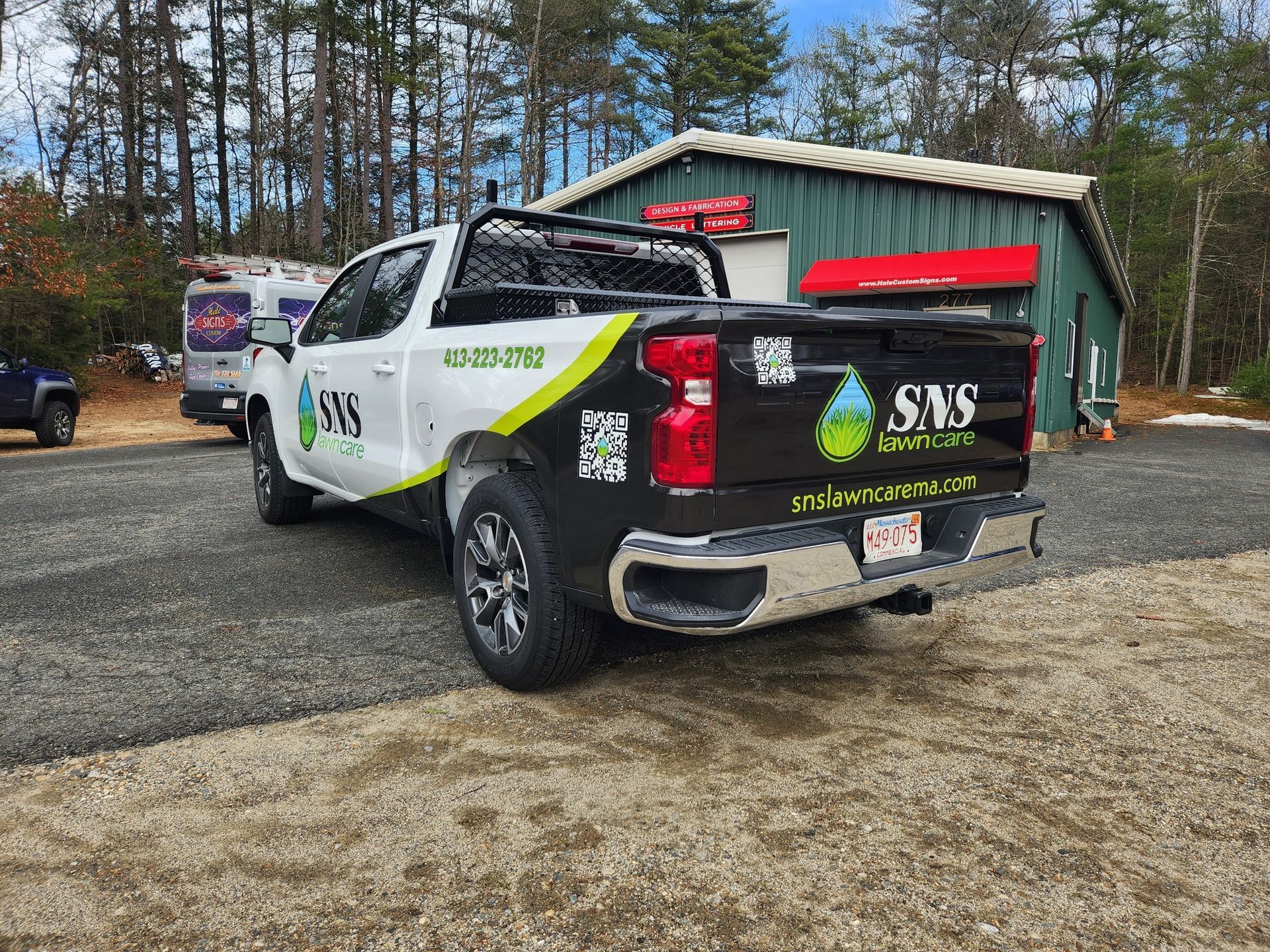 White service truck with company logo parked in gravel lot. Green building and trees in background.