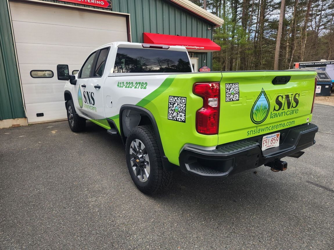 White truck with green and white company logo parked on gravel in front of a building.
