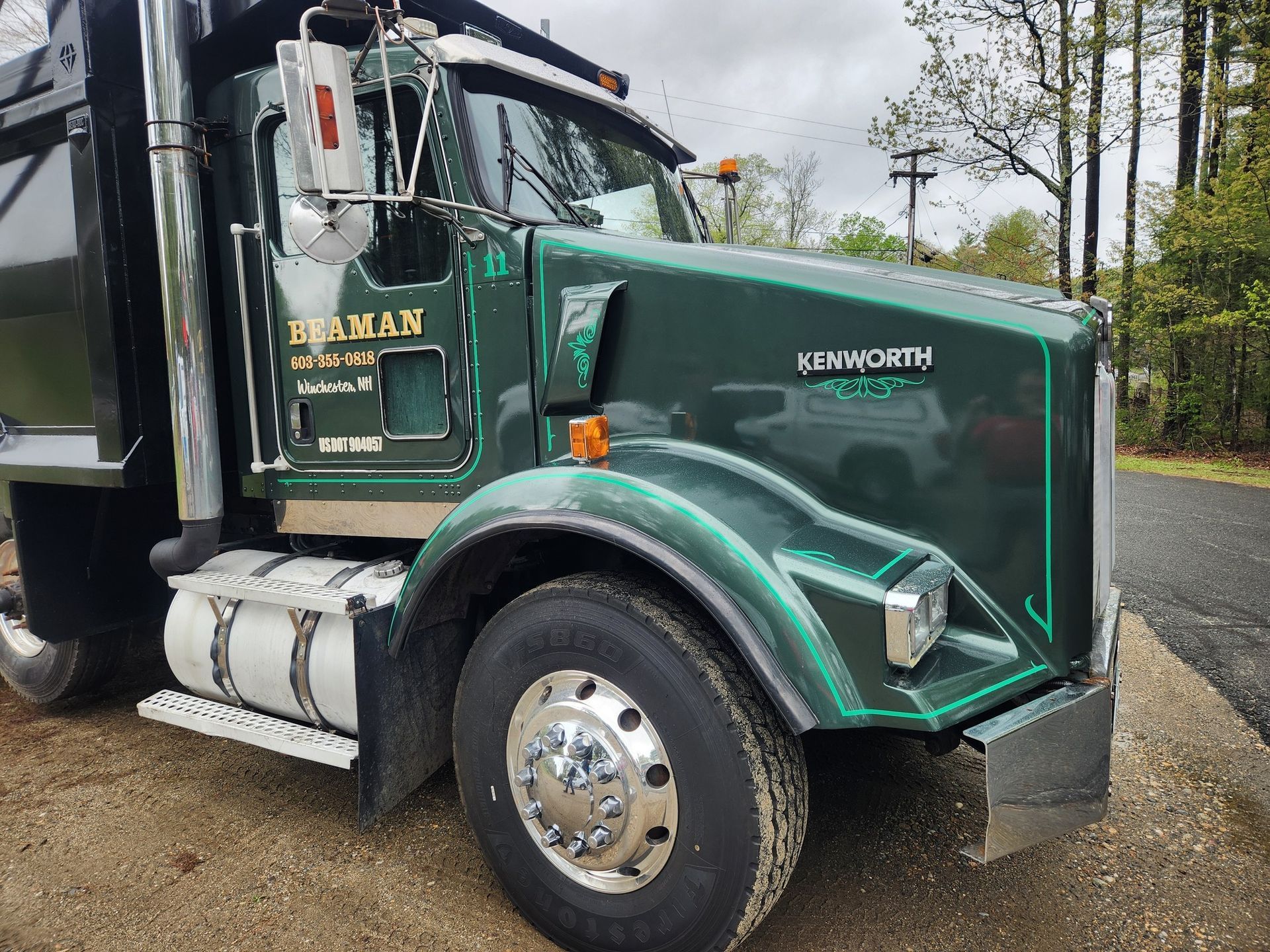 Green Kenworth dump truck parked on a road. 