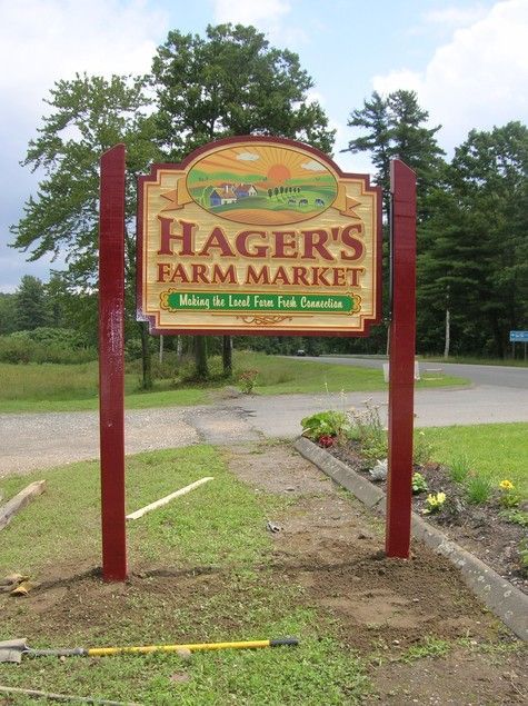 Hager's Farm Market sign; red posts, painted logo with farm scene and text on green.