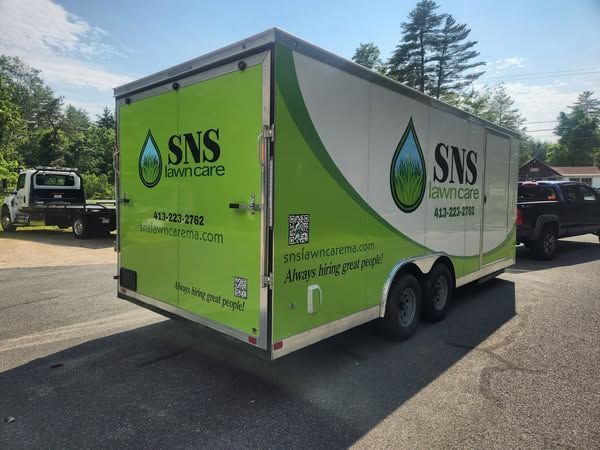 Green and white SNS Lawn Care trailer with logo, parked on a road.