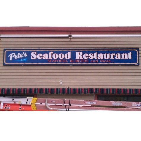 Sign for Pete's Seafood Restaurant, blue and white lettering on a brown building. Includes seafood, burgers, and more.