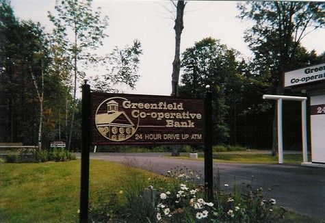 Sign for Greenfield Co-operative Bank with a 24-hour drive up. Set in a grassy area, surrounded by trees.