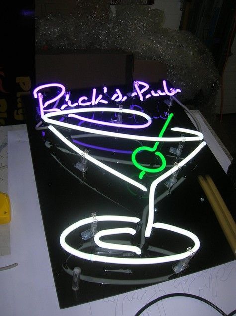 Neon sign for Rick's Pub; white and purple martini glass with a green olive; lit in a dark room.