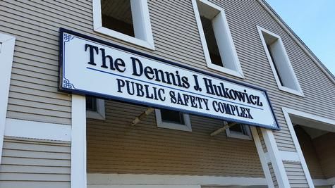 Sign for Dennis J Rukowicz Public Safety Complex on a two-story beige building.