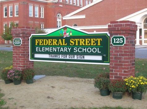 Sign for Federal Street Elementary School with brick pillars, green lettering, and flowers.