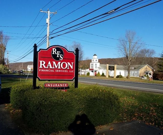 Sign for Ramon Financial Services, Inc. with a red and black color scheme, on a sunny roadside.
