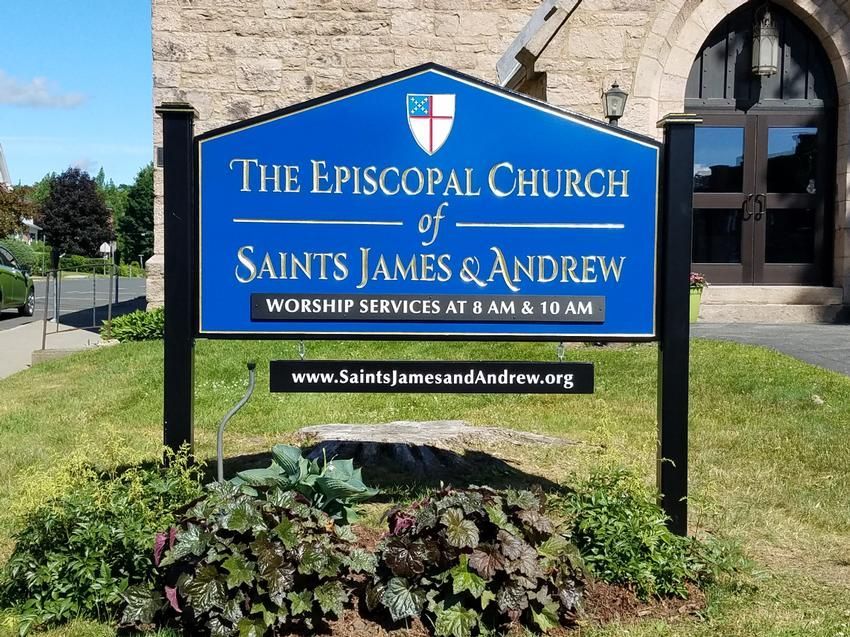 Sign for The Episcopal Church of Saints James & Andrew, blue and white, on green grass.
