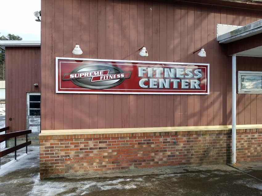 Supreme Fitness Center sign on a brown building with red brick and a white border.