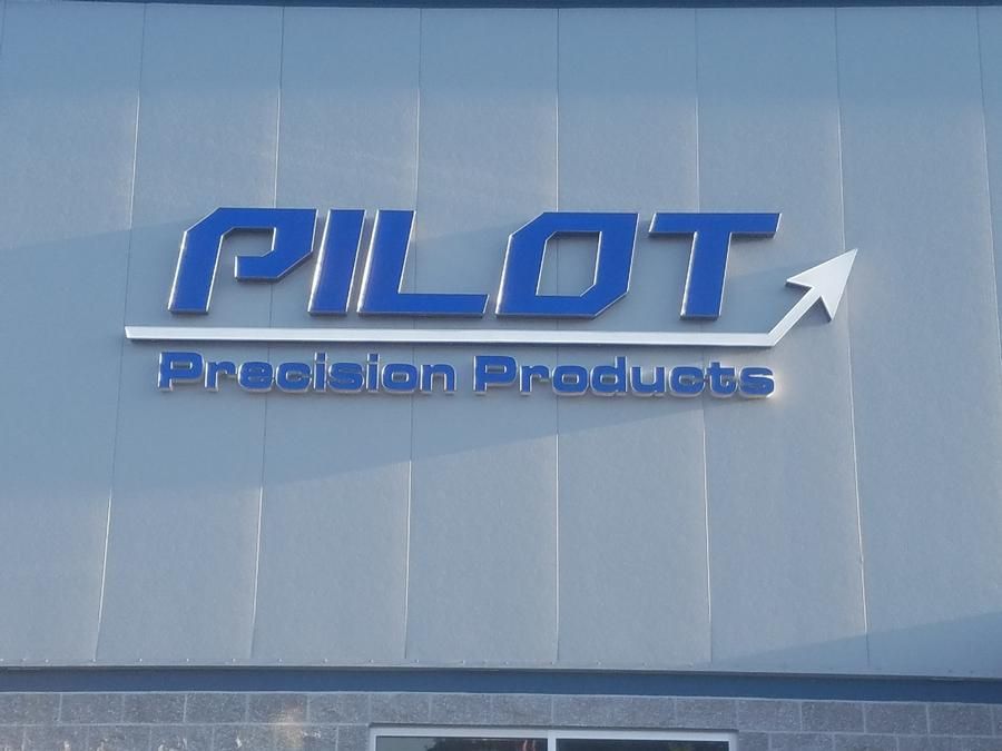 Pilot Precision Products sign in blue on a grey building; white arrow pointing up.