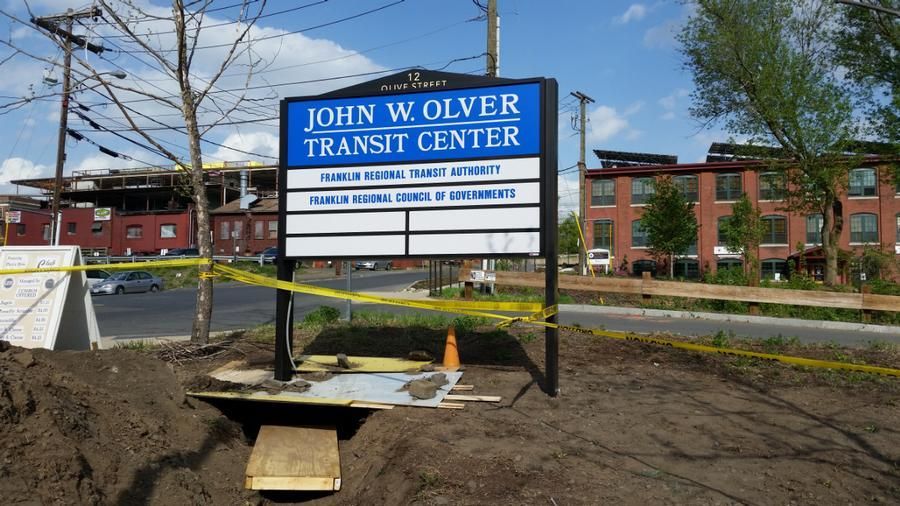 John W. Olver Transit Center sign, blue with white text, in front of a brick building under a blue sky.