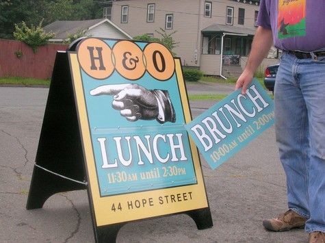 Man changing a sandwich board sign at H&O restaurant on Hope Street. Adding