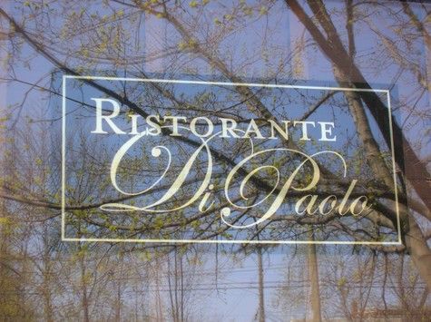 Ristorante Di Paolo sign on a window with a tree and blue sky in the background.